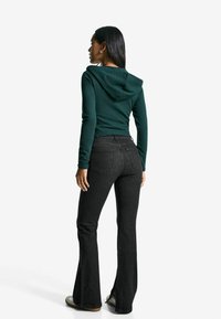 Dunkelgrüner, figurbetonter Hoodie mit Kapuze, kombiniert mit hochtaillierten, ausgestellten schwarzen Jeans. Glatte Textur und maßgeschneiderte Passform.