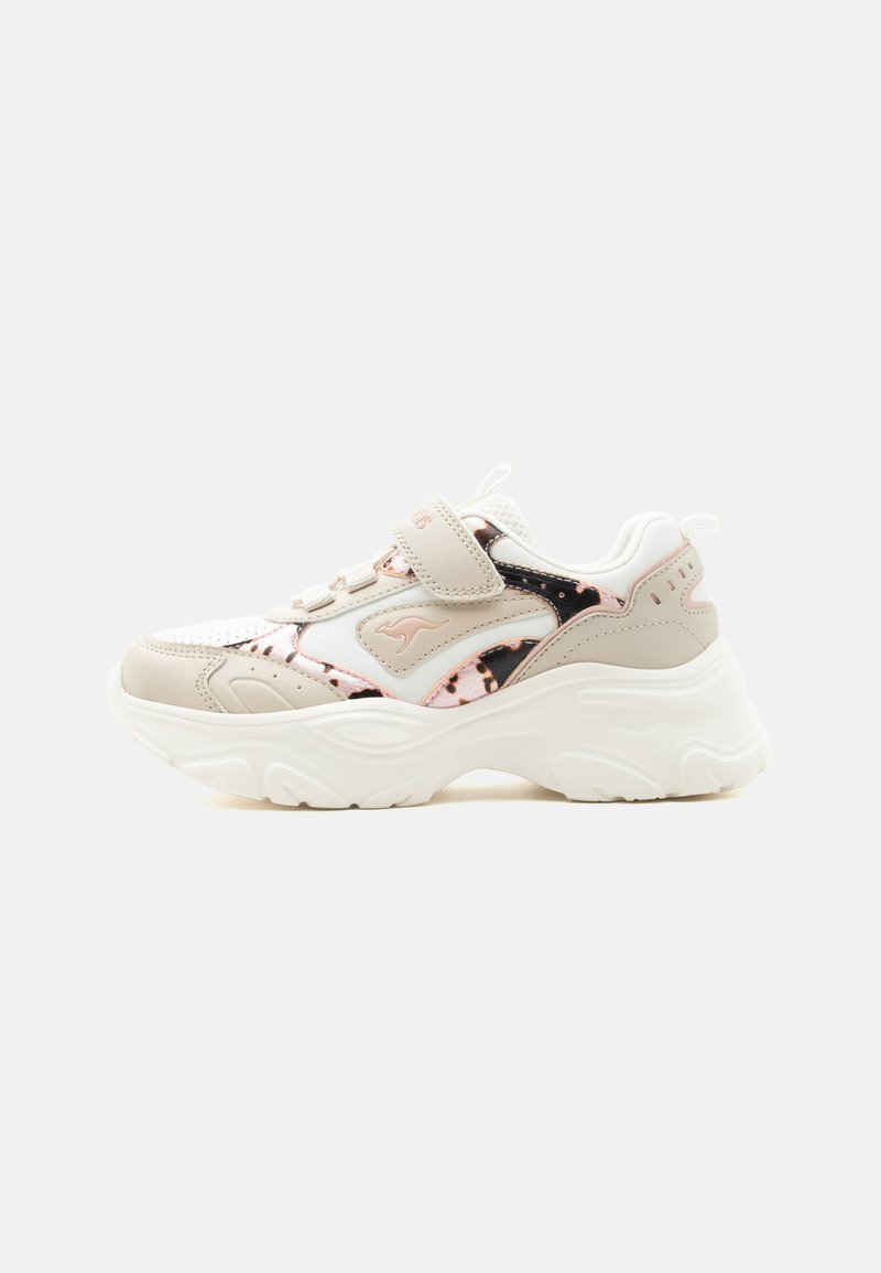 Baskets épaisses blanches et beige avec une semelle épaisse, une sangle velcro et des accents métalliques or rose et noir, présentées sur un fond uni.