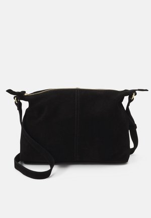 Sac bandoulière en daim noir avec fermeture éclair dorée, sangle ajustable et détails de nœuds latéraux, présenté sur fond blanc.