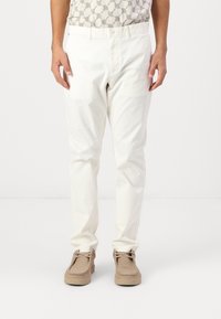Pantalon en coton blanc à coupe droite, fermeture à bouton classique et poches, associé à des chaussures en daim beige. Design minimaliste.