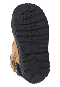 Zwarte rubberen zool met een profiel voor grip, met de woorden "FLEX SYSTEM" en "GEOX." Bovenkant is gemaakt van tan suède met marineblauwe accenten en heeft een ritssluiting.