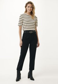 Stickad topp med svarta zigzag-ränder på en krämfärgad bakgrund, kombinerad med högmidjade svarta byxor och svarta klackiga ankelstövlar.