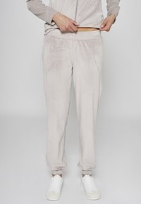 Jasnobeżowe spodnie dresowe z miękkiego welurowego materiału, z elastycznym pasem, bocznymi kieszeniami i ściągaczami przy kostkach. Noszone z białymi sneakersami.