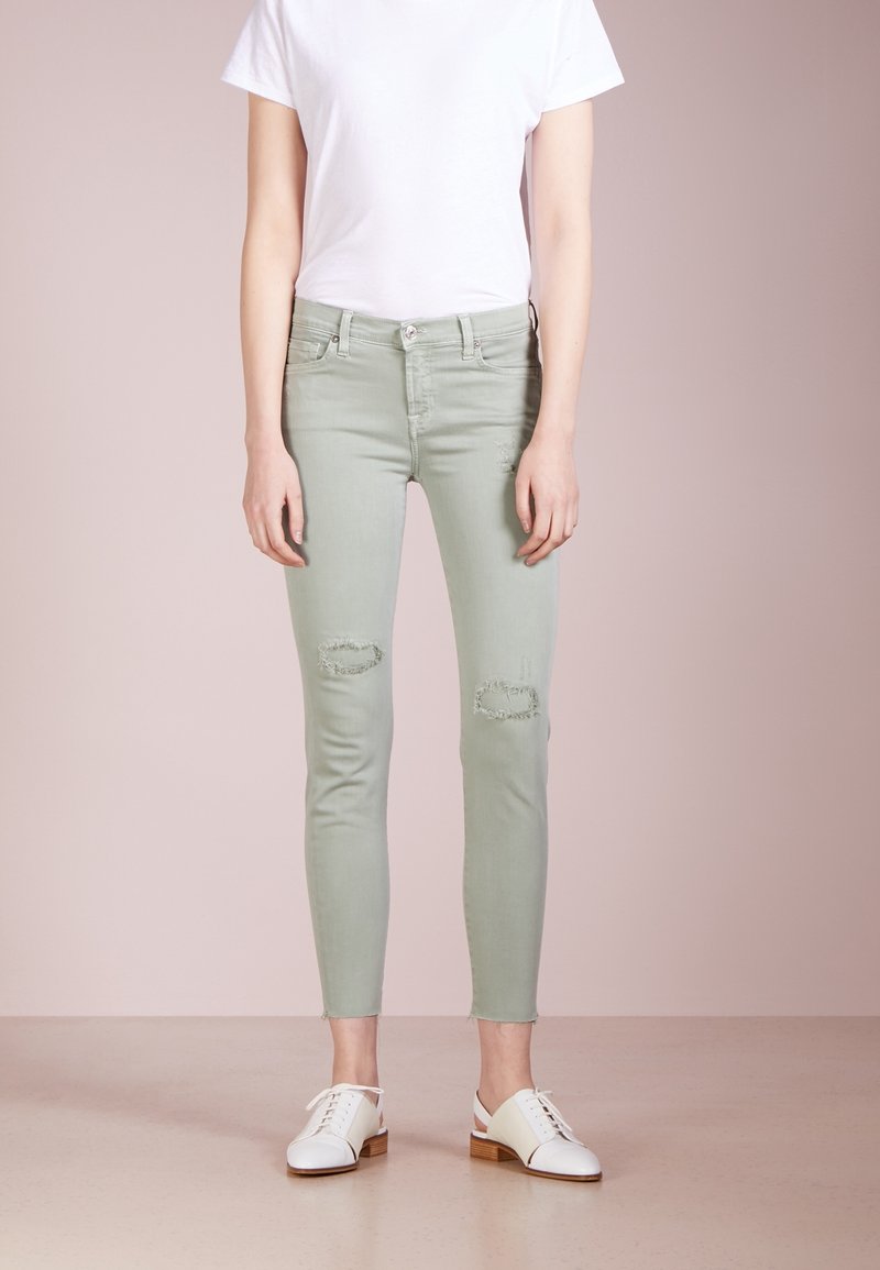 Vaaleanvihreät kapeat farkut, joissa on kuluneet polviyksityiskohdat, yhdistettyinä yksinkertaiseen valkoiseen T-paitaan ja valkoisiin kenkiin, joissa on puukorot.