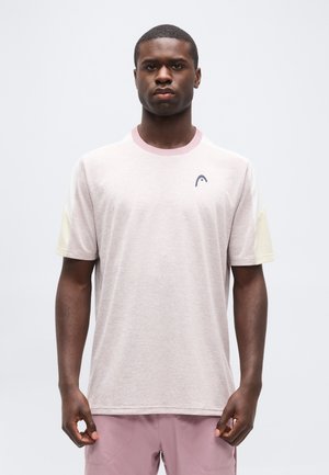 Man draagt een lichtroze en crèmekleurig shirt met korte mouwen en een klein logo op de borst, staand tegen een effen witte achtergrond.