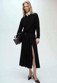 Maglione nero a maglia con colletto bianco, abbinato a una gonna midi nera plissettata con uno spacco laterale e accessoriate con una borsa scura.