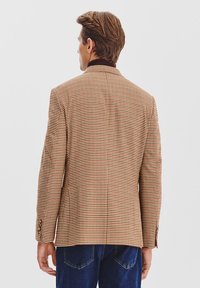 Brązowa i kremowa marynarka w kratę z wywiniętym kołnierzem, zapięciem na dwa guziki i teksturowanym materiałem. Posiada boczne wentylacje i mankiety zapinane na guziki.