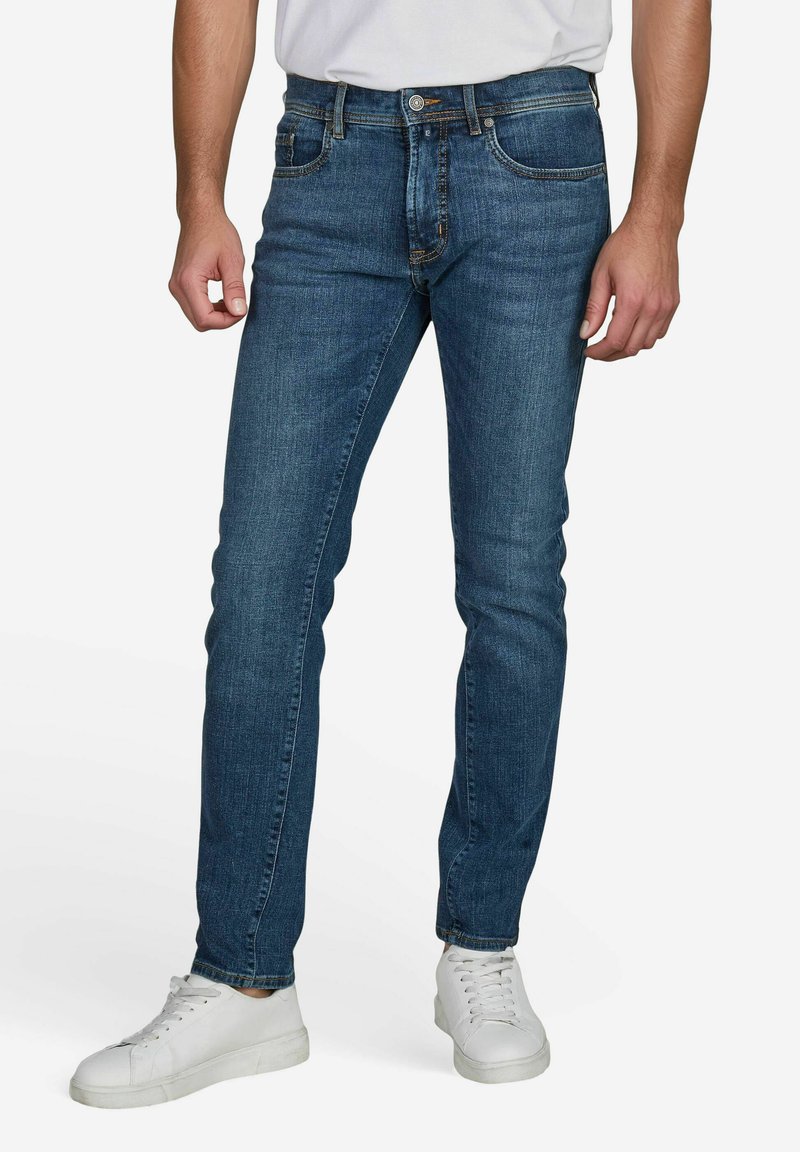 Dunkelblaue Jeans mit schlanker Passform, aus Denim gefertigt, mit Fronttaschen, dezenten Waschungen und weißen Sneakern als Kontrast.