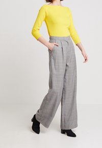 Gul långärmad topp i kombination med högmidjade, grå rutiga vida byxor. Byxorna har framfållningar och sidfickor.