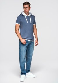 Modrá mikina s krátkým rukávem a bílou podšívkou, vybavená stahovací šňůrkou. V kombinaci s světle modrými džíny a bílými teniskami.