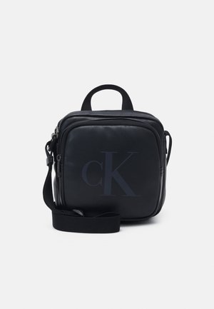 Schwarze Leder-Umhängetasche mit quadratischem Design, oberem Griff, verstellbarem Riemen und einem dezenten "CK"-Logo auf der Vorderseite.