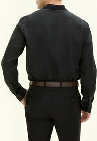 Maglietta nera a maniche lunghe con una texture liscia, colletto e polsini abbottonati, indossata con pantaloni neri aderenti e una cintura in pelle marrone.