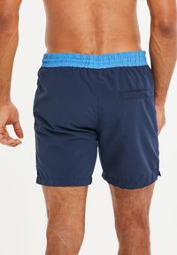 Marine zwemshorts met een lichtblauwe elastische tailleband. Heeft een achterzak en een lichte, gladde stof. Lengte tot boven de knie.