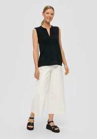 Black sleeveless top with a V-neck, paired with white wide-leg pants and black platform sandals. The outfit features clean lines and contrasting colors.
