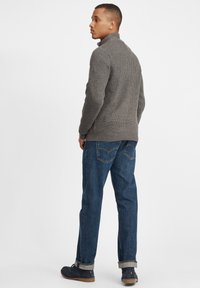 Grau gestrickter Pullover mit hohem Kragen, kombiniert mit blauen Jeans aus Denim. Die Jeans haben eine lässige Passform und sichtbare Gesäßtaschen.