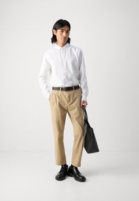 White button-up shirt, beige trousers, black belt, and black shoes. Carrying a black tote bag. Simple design, neutral color palette.