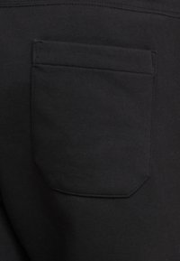 Svart tyg med slät textur, med en enda fyrkantig bakficka med rundade hörn och synlig sömdetalj.