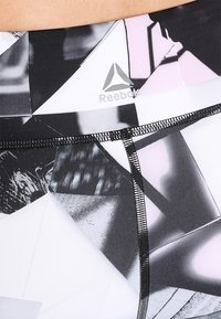 Reebok leggings med ett geometriskt mönster i svart, vitt och rosa, med en slät textur, elastisk midja och svarta sömnadsdetaljer.