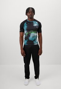Short-sleeve athletic shirt featuring a black base with blue and green tie-dye patterns, complemented by black pants and white sneakers.