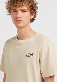 T-shirt in cotone beige a maniche corte, con logo O'Neill ricamato in nero sul lato sinistro del petto. Tessuto morbido, vestibilità rilassata.