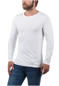 Camiseta blanca de manga larga hecha de material de algodón suave, con un escote redondeado y un diseño ajustado. Combinada con jeans de mezclilla azules.