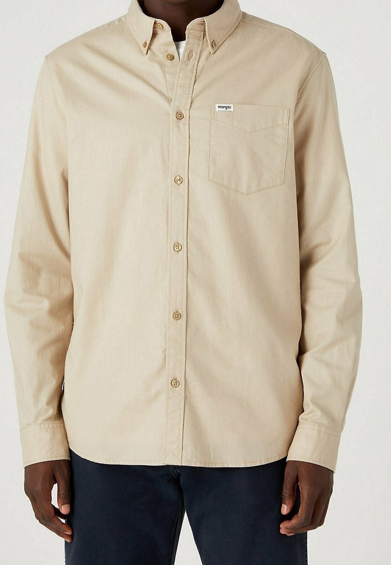 Camicia beige con bottoni, colletto, tasca sul petto e bottoni marroni a contrasto. Realizzata in tessuto liscio, con maniche lunghe e taglio ampio.