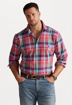 Rutig skjorta i röd och blå med långa ärmar, knapplösning, bröstficka och krage, tillsammans med denimjeans och ett brunt bälte.