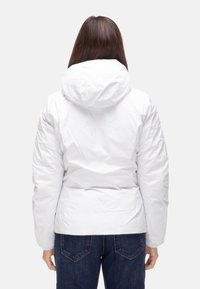 Giacca impermeabile bianca con chiusura frontale con cerniera, cappuccio regolabile e imbottitura, abbinata a jeans di denim blu scuro.