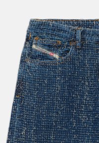 Jeans en denim bleu foncé avec texture effilochée. Comprend une étiquette de marque, une fermeture à bouton en métal et des accents de couture orange.