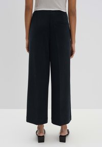 Pantalons à jambes larges en tissu bleu marine foncé, présentant une texture lisse, deux poches arrière et un ourlet net pour une finition soignée.