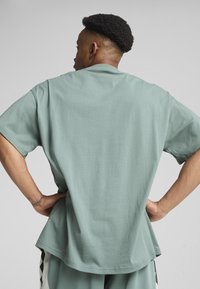 Mintgrünes, übergroßes T-Shirt mit kurzen Ärmeln, strukturiertem Stoff, abgerundetem Saum und lässiger Passform, getragen mit Händen auf den Hüften.