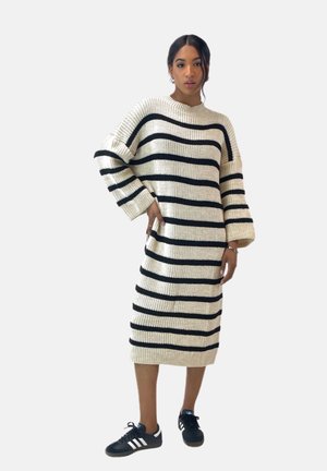 Strikket kjole med creme- og sorte vandrette striber, der har ribbet hals, oversized ærmer og længde til midt på læggen. Bruges med sorte sneakers.