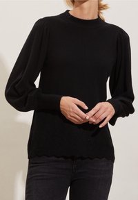 Pull noir avec manches bouffantes longues, col côtelé et ourlet festonné. Présente un motif texturé en bas. Matière en tricot douce.