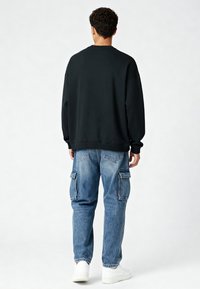 Fekete, hosszú ujjú pulóver lazább szabással, világoskék cargo farmerral, oldalsó zsebekkel és szűkülő lábbal, fehér sportcipővel kombinálva.