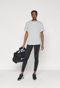 Graues Nike-T-Shirt, schwarze Leggings mit strukturierten Akzenten, schwarze Sportschuhe und eine schwarze Sporttasche mit doppelten Griffen.