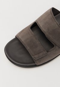 Gray suede sandal with two adjustable straps, smooth black sole, and cut-out design for breathability. Textured surface and stitch detailing.