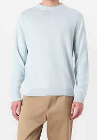 Ljusblå stickad tröja med ribbad rund halsringning och muddar, med en avslappnad passform, gjord av mjukt material, kombinerad med beige byxor.