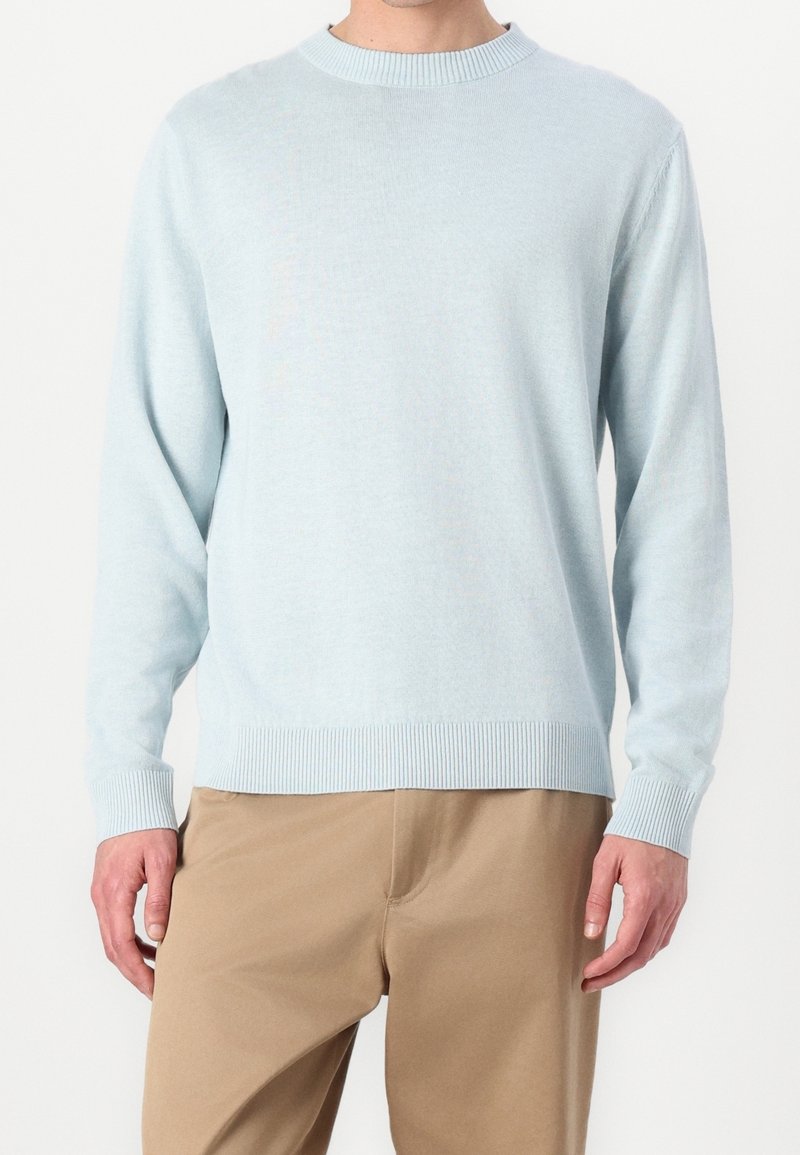 Ljusblå stickad tröja med ribbad rund halsringning och muddar, med en avslappnad passform, gjord av mjukt material, kombinerad med beige byxor.