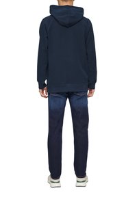 Sudadera azul marino con capucha, puños y dobladillo acanalados, combinada con jeans de un azul oscuro. El atuendo se completa con zapatillas blancas y verdes.