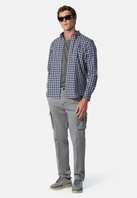 Camisa de cuadros en azul marino y blanco, cuello redondo gris debajo, pantalones cargo grises y zapatillas grises con acentos verdes.
