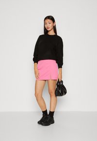Schwarzer Pullover, rosa Miniröcke mit seitlichem Schlitz, schwarze Knöchelsocken, schwarze klobige Schuhe und eine schwarze geraffte Handtasche. Einfache Farbkontraste.