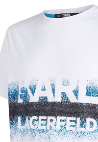 Bílý bavlněný tričko s velkou grafikou, která zobrazuje slova "KARL" a "LAGERFELD" v tučném, černém a modrém skvrnitém designu. Kulatý výstřih.