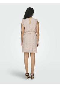 Lichtroze kort jurkje met bloemen uitsparingen, gerende schoudermouwen en een keyhole rugdetail, afgewerkt met een ceintuur in de taille.