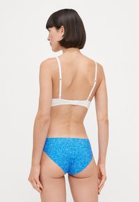 Wit gemerkt bikini-top en blauwe patroon bottom, met verstelbare schouderbanden en gladde texturen, van achteren getoond.