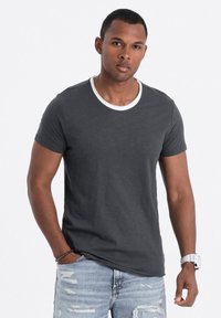 T-shirt grigio scuro a maniche corte con scollatura tonda bianca, abbinato a jeans chiari strappati. Il tessuto appare morbido e leggero.