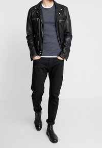 Black leather biker jacket over a gray sweater, paired with black tapered pants and black ankle boots. Features zippers and rolled cuffs.