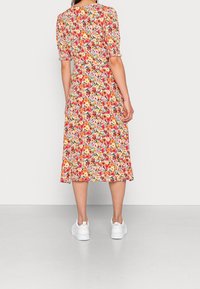 Blommig midi-klänning med korta puffärmar, prydd med ett färgglatt blommönster på en ljus bakgrund, kombinerad med vita sneakers.