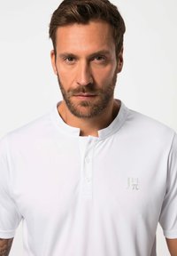 Polo bianco con colletto corto e aperto, placket a due bottoni e un logo discreto sul petto. Realizzato in tessuto liscio con un design aderente.
