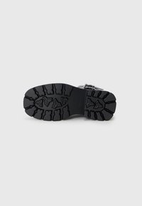 Black rubber boot sole with a textured, rugged tread pattern for traction, featuring an asymmetric design and reinforced edges.