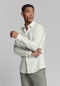 Lichtgroen overhemd met knopen in een linnenmix, voorzien van een kraag, lange mouwen en bruine knopen. Gecombineerd met lichtgrijze broek.